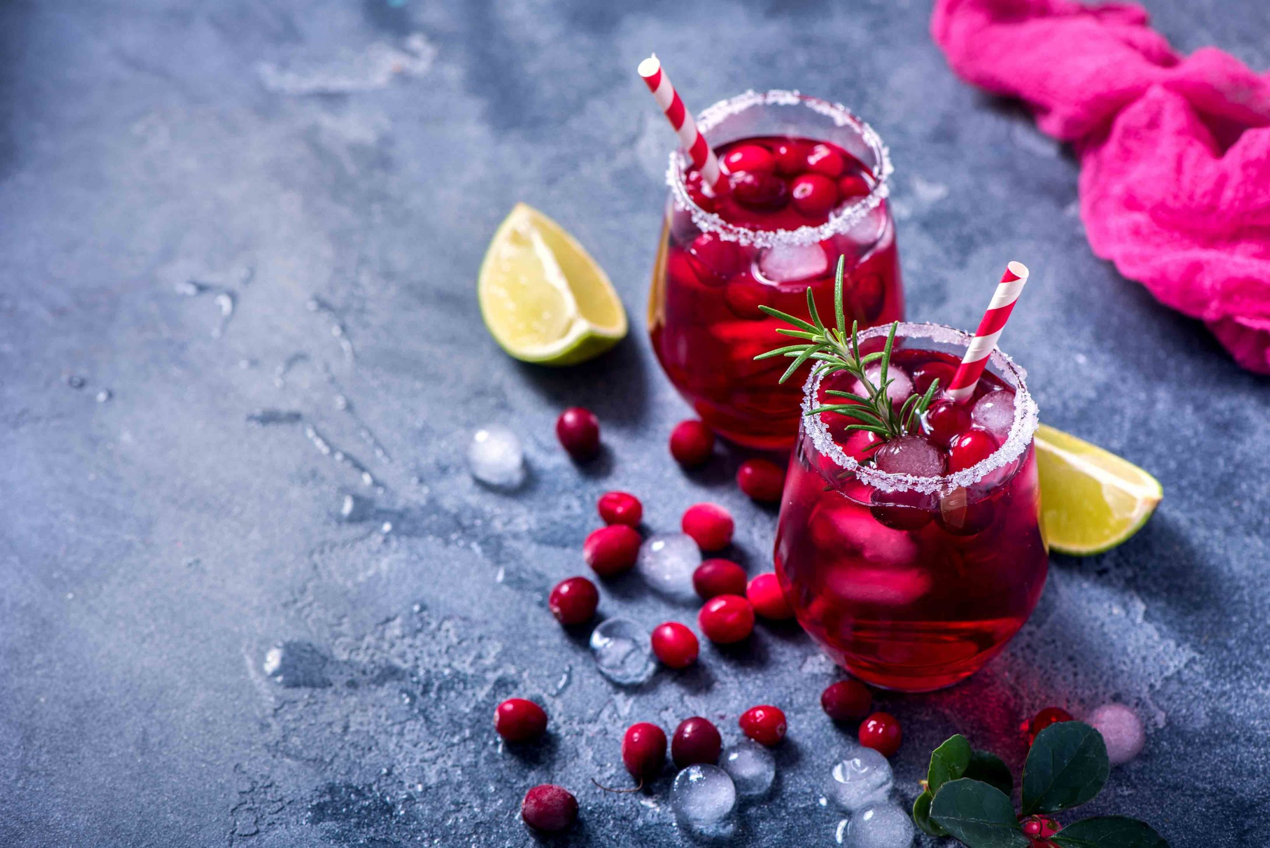 Two glasses of cranberry juice with lime and ice.