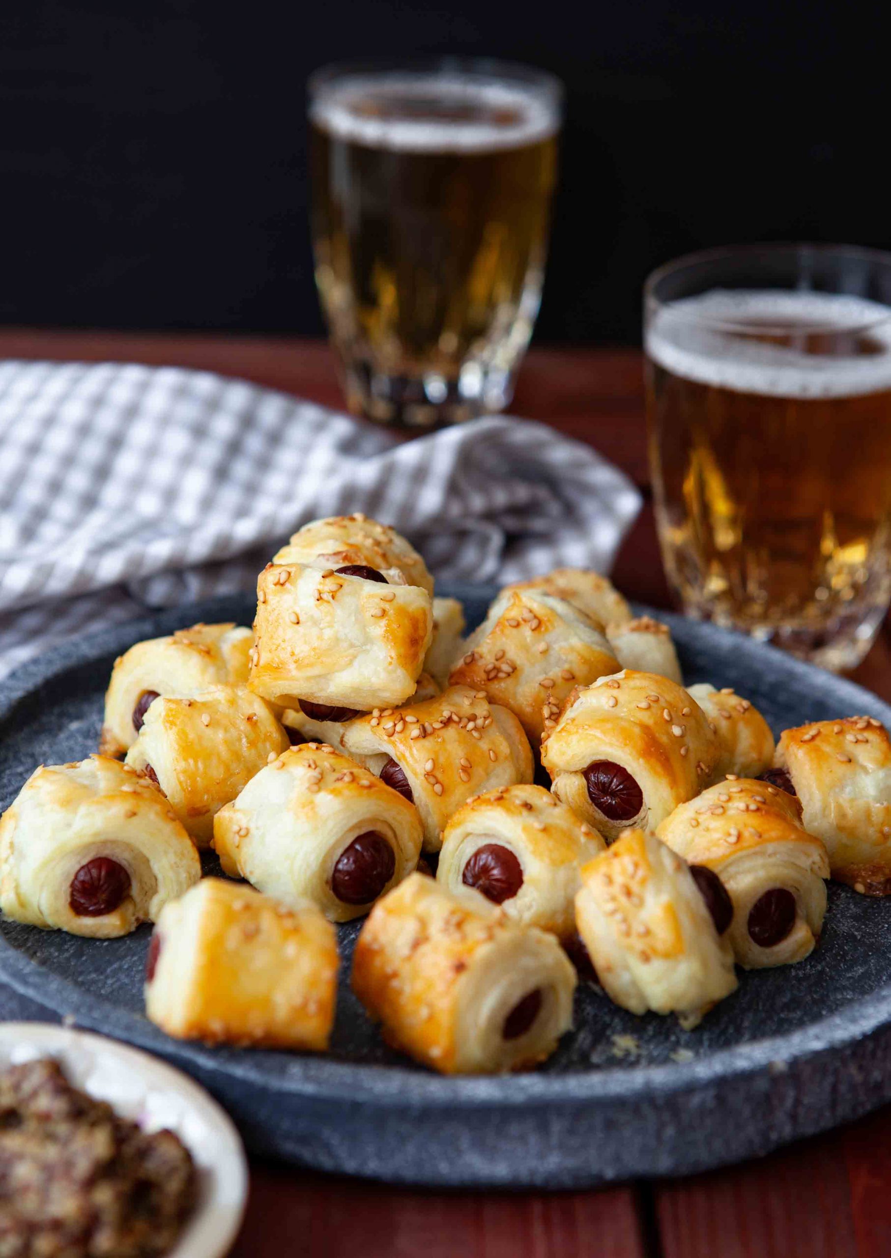 Sausage rolls on a plate next to a glass of beer.